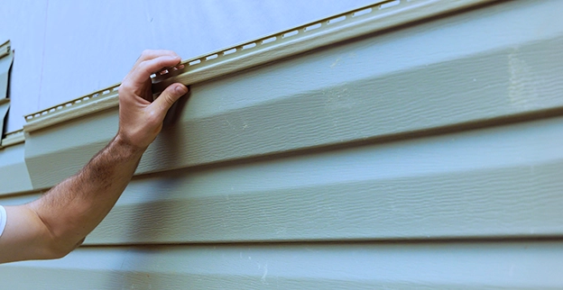 A person installs brown siding on a home.